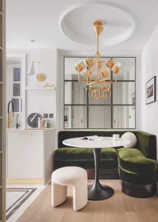 A plush green velvet breakfast nook nestled into the corner of a pale cream kitchen.