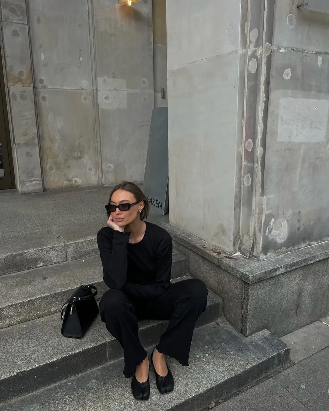 A woman wears black Tabi shoes with black jeans on the stairs