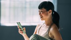 Woman holding yoga mat for dead bugs, looking at phone and smiling