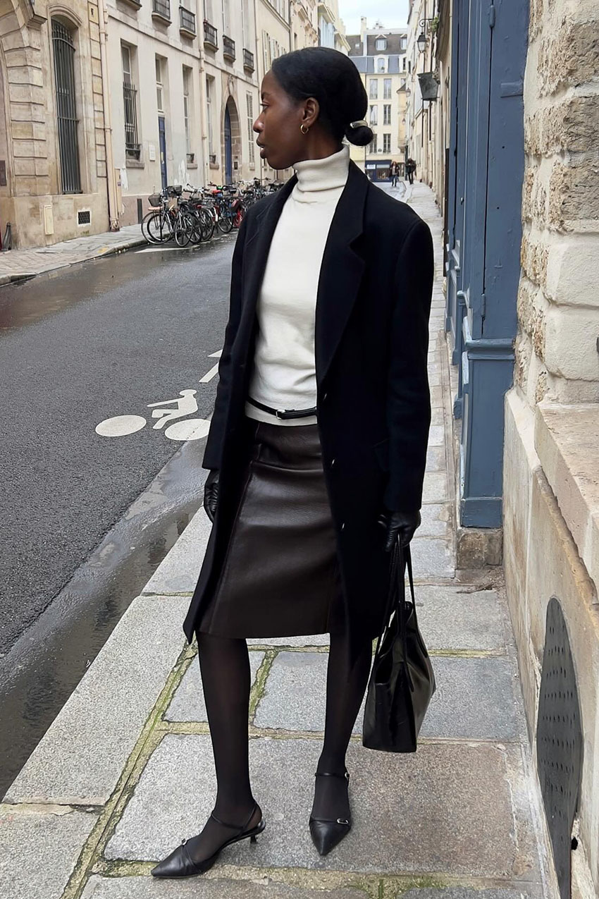 a woman wearing a turtleneck, black cardigan, and black leather skirt