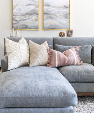 Gray sectional with throw pillows in different colors and textures, area rug on floor and white wall with artwork behind