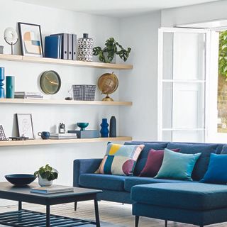 Living room with blue sofa and cushions and white shelves along wall.