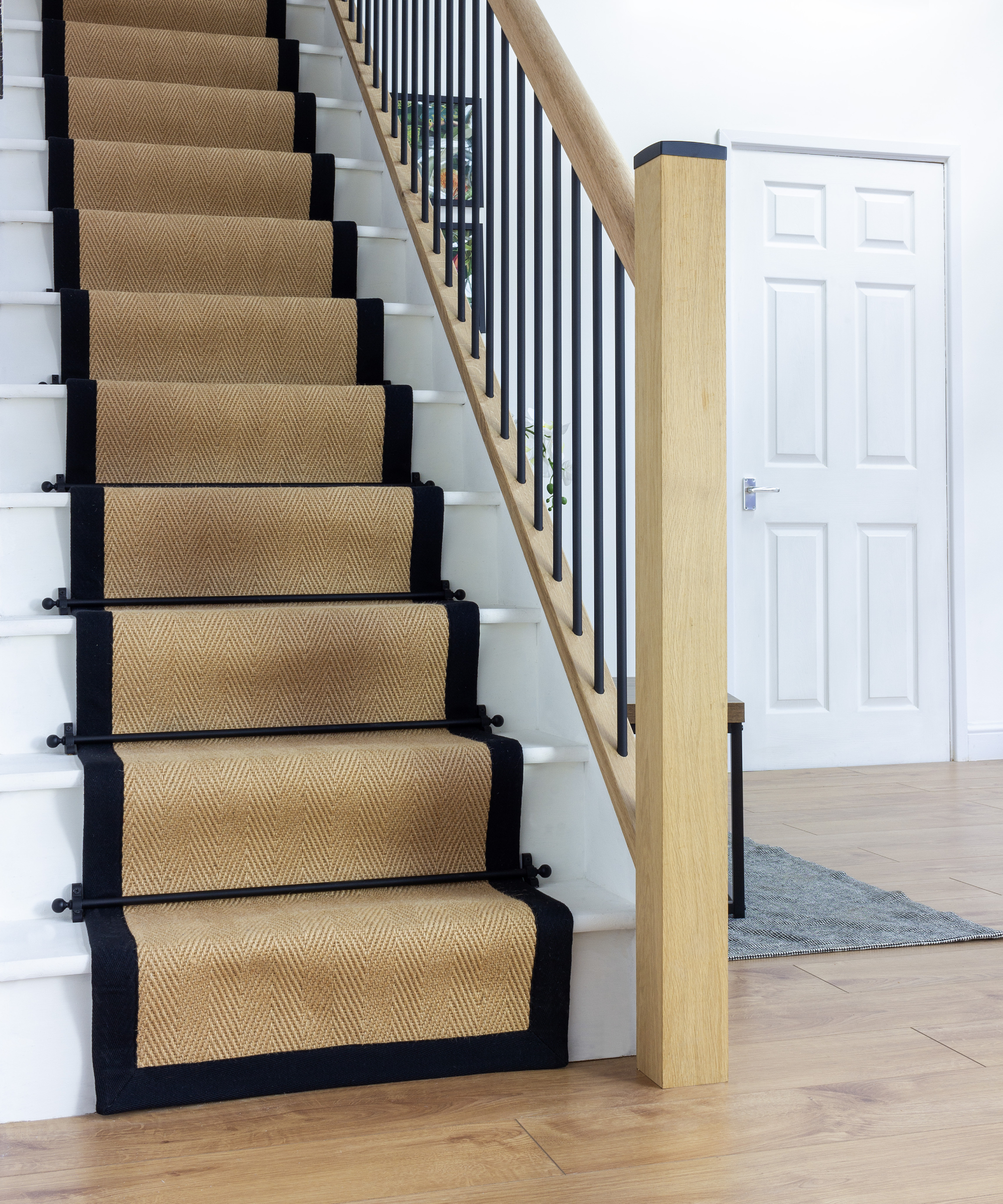 straight staircase with black edged sisal stair runner, modern wooden handrail, black spindles