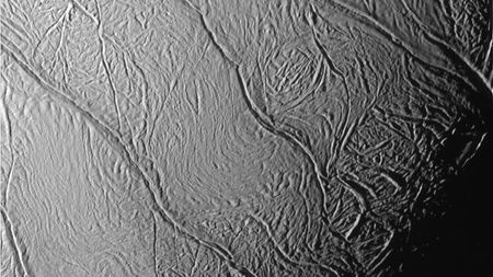 a close up view of an icy moon of saturn showing deep fissures along its surface