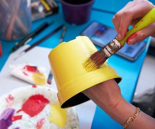 Hands painting a planter bright yellow