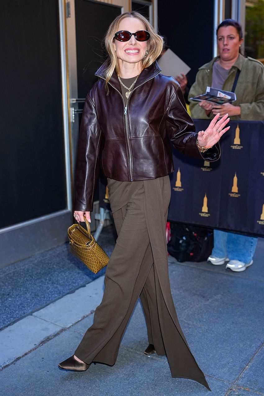 Kristen Bell wearing a brown leather jacket, sash pants, and satin pumps in NYC