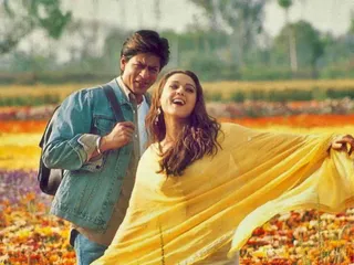 a woman in a yellow shall sings to a man in a denim jacket in a flower field in veer zaara