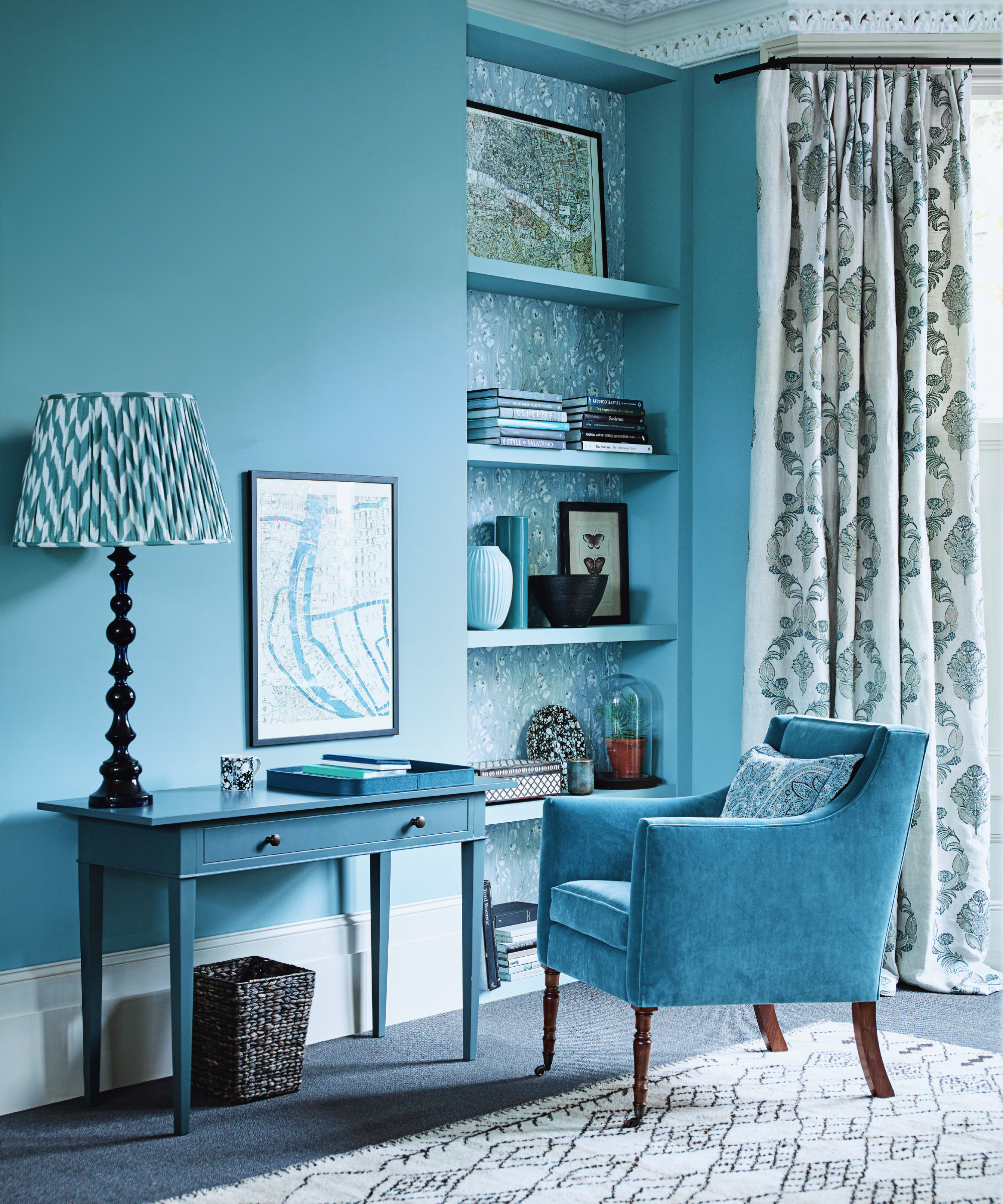 colour drenched blue living room with blue walls, open alcove shelving, blue chair, console desk and table lamp