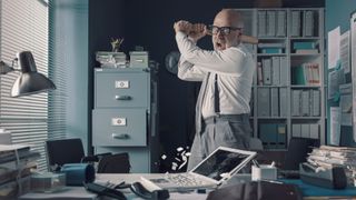 stressed businessman destroying his desk and laptop with a baseball bat