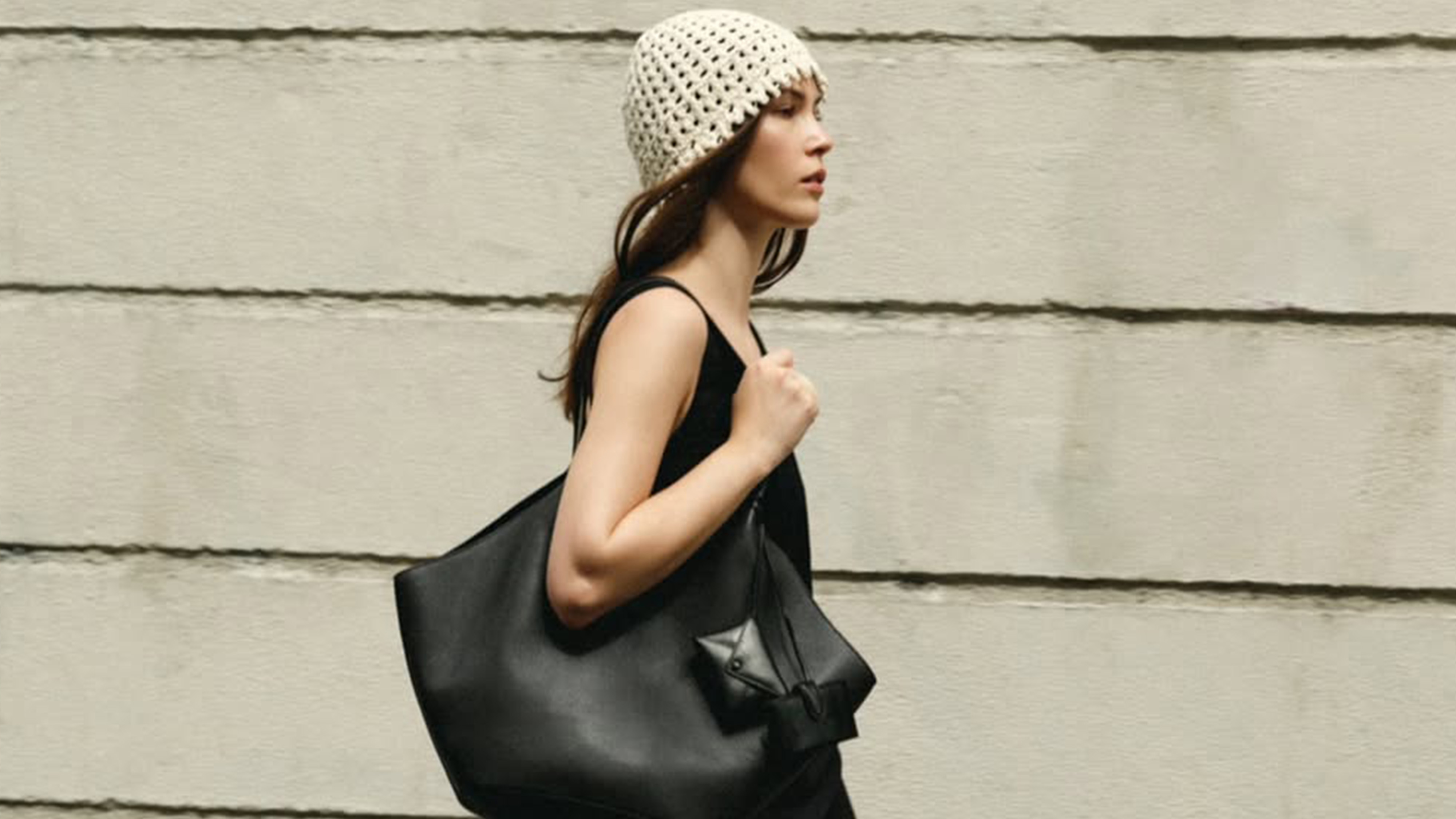 Lena wears a crochet hat, black tank top, and black tote bag.