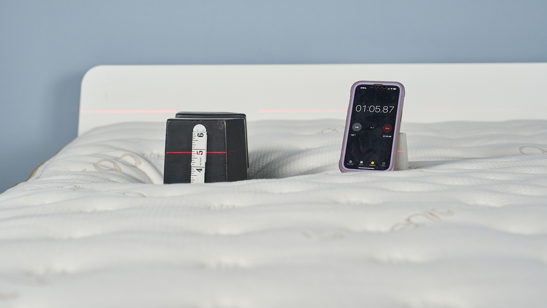 Image shows the highest weight in our pressure relief weighted indentation test being placed on top of the Saatva Classic: a 25kg cast iron weight placed in the shoulder area, which is a key impact zone on the body when side sleeping and back sleeping. A measuring tapes gives us a visual record of how much the mattress is indenting at that spot under the 25kg weight.