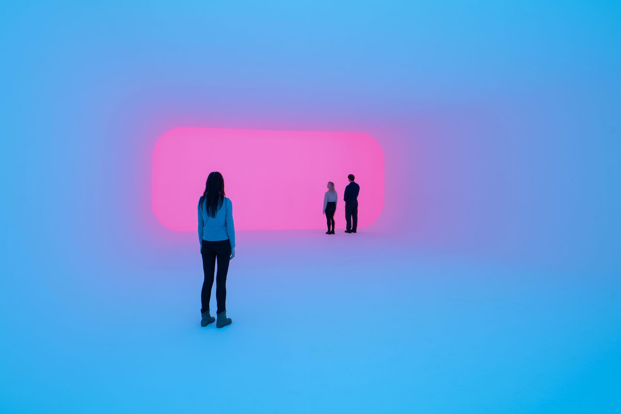 James Turrell, Aftershock Light &amp; Space features three people (one standing back) looking towards a purple light. 