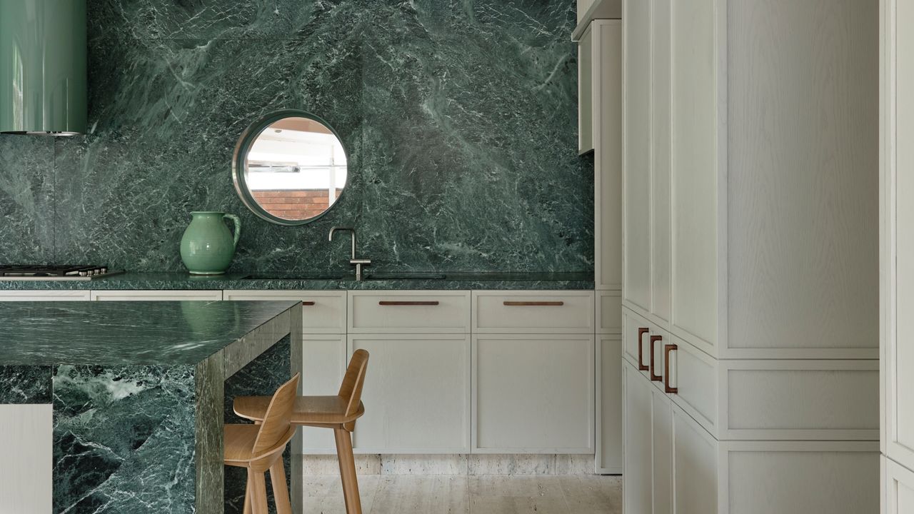 White kitchen with green stone units and walls and porthole window looking to outside