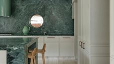White kitchen with green stone units and walls and porthole window looking to outside