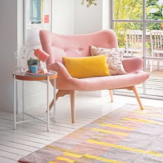 Living room with white floorboards, a rug and pink armchair.