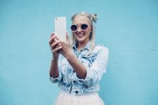 Happy fashionable young woman talking selfie against blue wall
