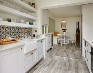 A white galley kitchen with patterned tiles splashback, white countertop and dining table area