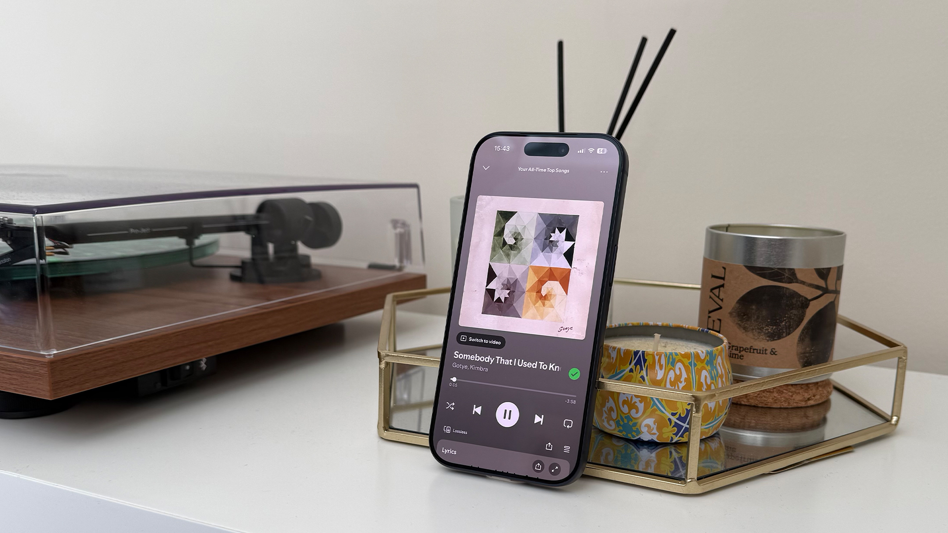 Apple iPhone 17 Pro smartphone leaning upright next to record player, on screen is Spotify player