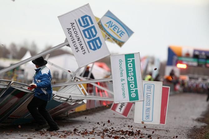 A man tries to stand up some signs which blew over onto the course.