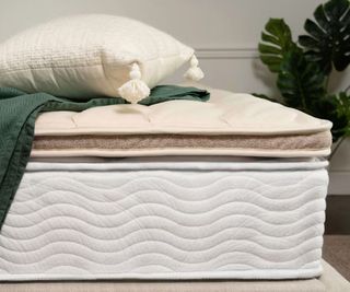 Saatva Organic Quilted Mattress Topper on a mattress with a pillow and a blanket.