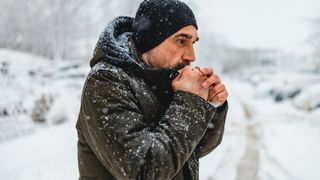 Man dressed in winter clothes outside in the snow holding his hands to his mouth
