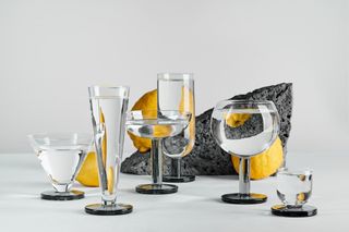 Drinking glasses by Tom Dixon, with rocks and lemons in the background. Included are clear glasses for water, champagne, wine and cocktails, they all feature a black glass base