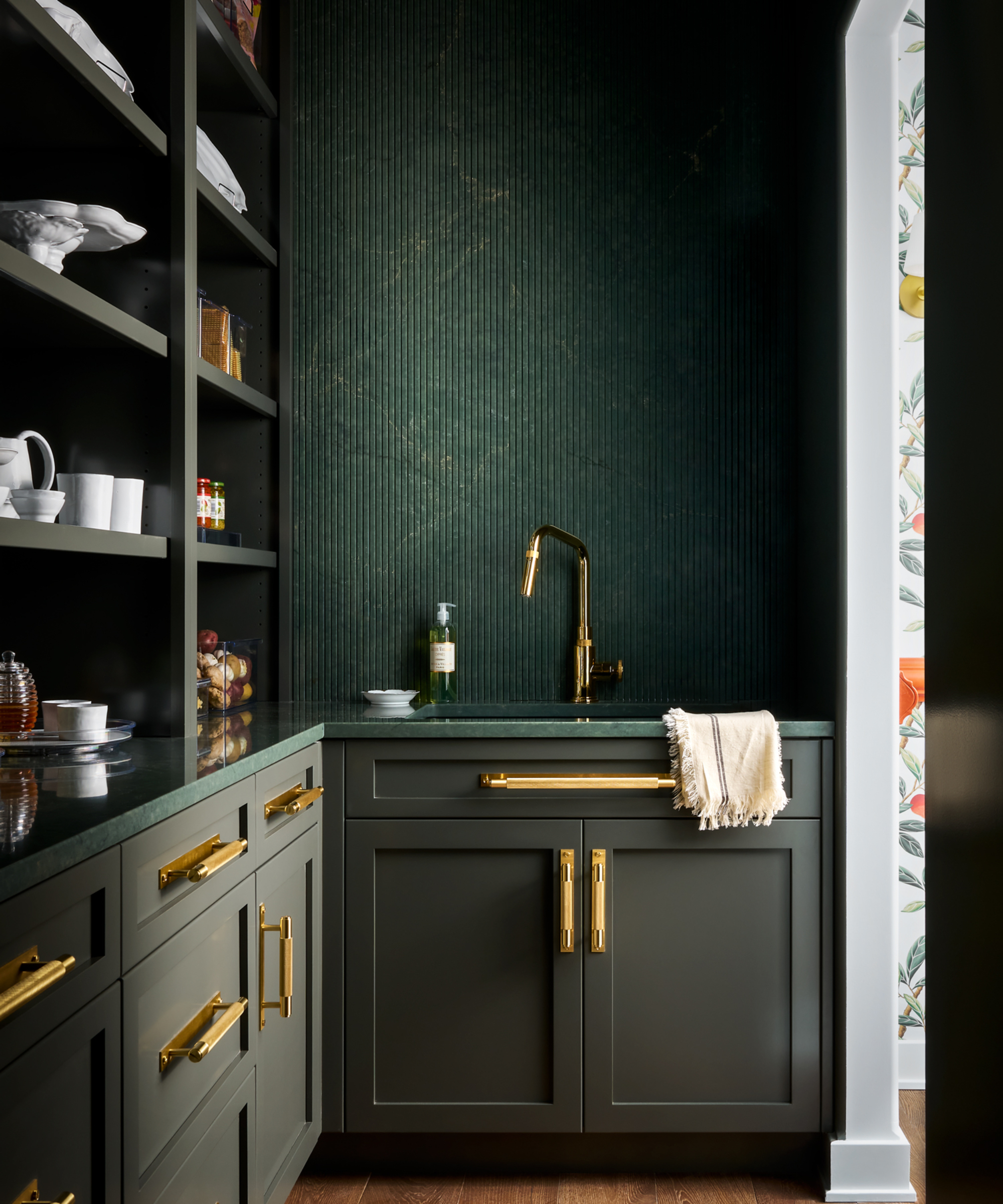 dark green painted walk in pantry with gold handles on cabinet and sink with gold tap