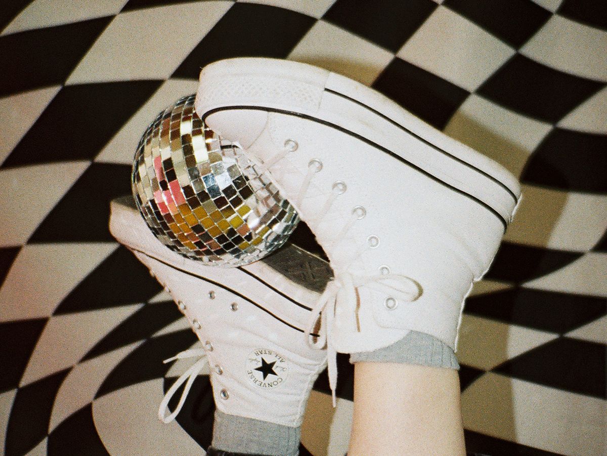 White Converse sneakers holding a small disco ball against a black and white checkered background