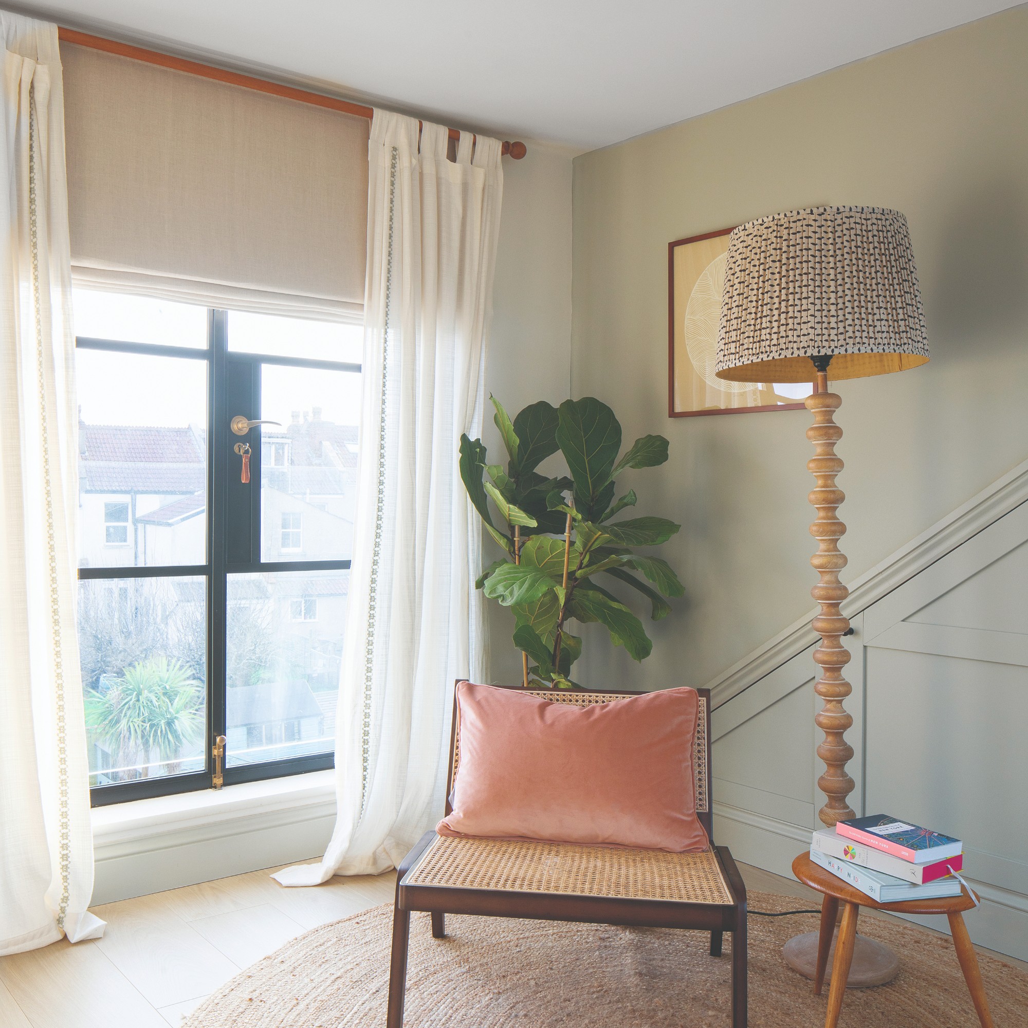 A reading corner by a large window dressed with white full-length curtains and blinds