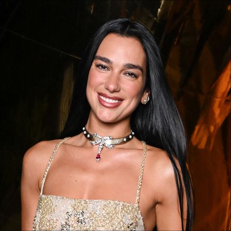 Dua Lipa wearing a gold floral vest top and smiling
