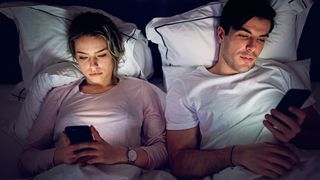 Couple sitting up in bed both using their smartphones