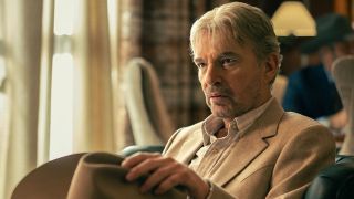Tommy (Billy Bob Thornton) sits wearing a smart beige suit and holding a Stetson hat in his left hand, his brown eyes gazing at someone off-screen in a still from Landman Season 2.