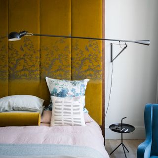 Bedroom with gold headboard and wall hung lamp