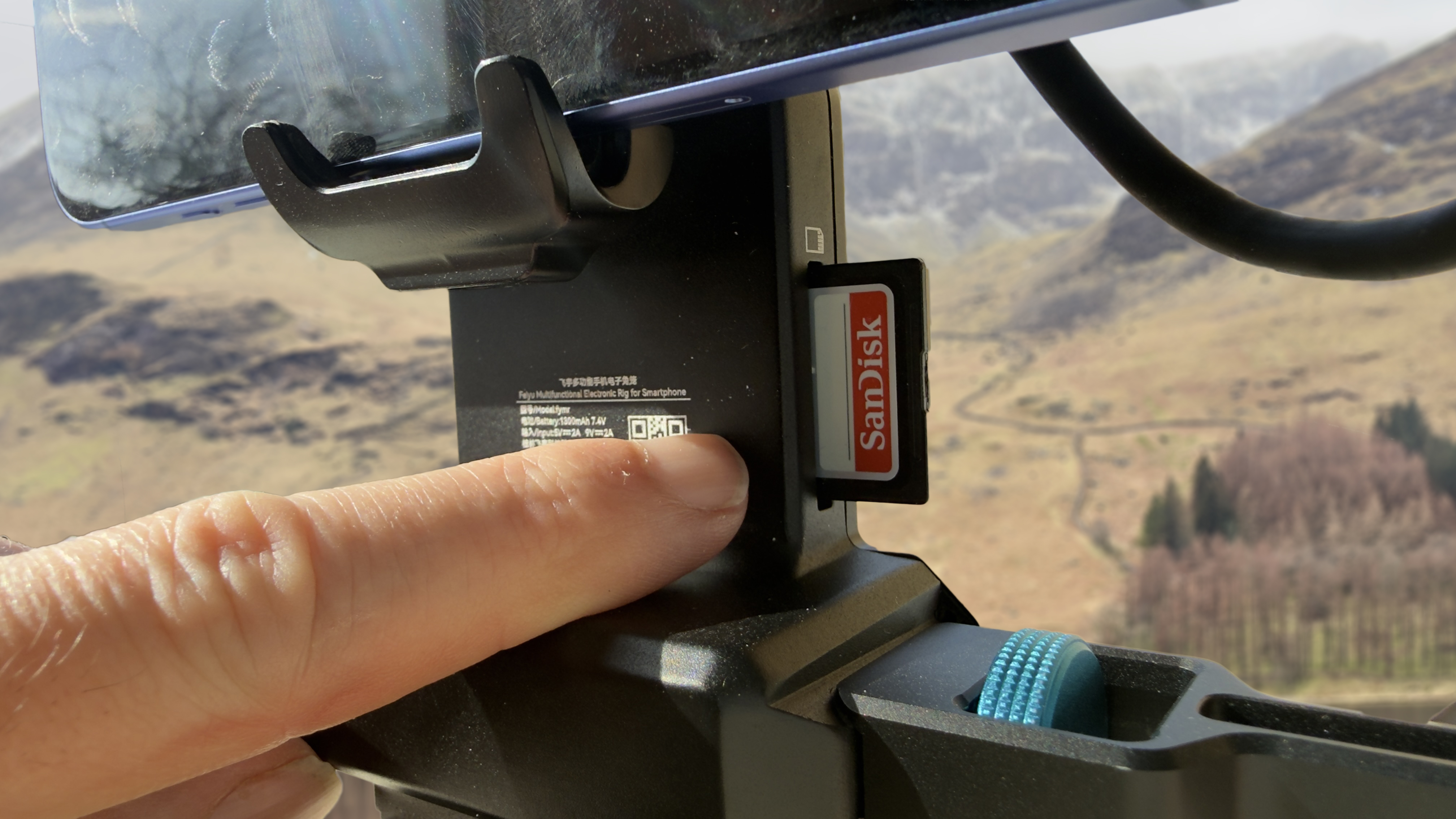 Smartphone mounted in a handheld video rig with a SanDisk SD card inserted into the rig&amp;rsquo;s built-in storage slot.