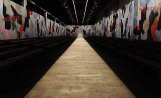 A catwalk decorated with futuristic murals, with the words 'Made in Italy' and overhead drone cameras