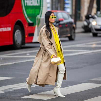 Miki Cheung seen wearing white boots, yellow oversized blazer, beige trench coat, over knees white bag, golden bag, neon sunglasses outside Acne during Paris Fashion Week - Womenswear F/W 2022-2023 on March 02, 2022 in Paris, France.