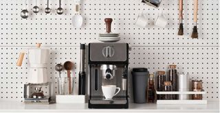Kicthen area with white pinboard wall with hanging utensils surrounding a coffee machine