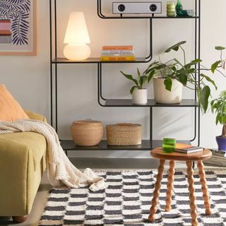 A black and white checkerboard rug sits in front of a couch and a metal shelving unit
