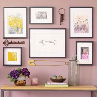 Gallery wall of artwork hung over a console table on a lilac wall