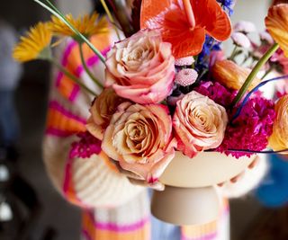 Multicolored flowers arranged in a vase being held by a woman