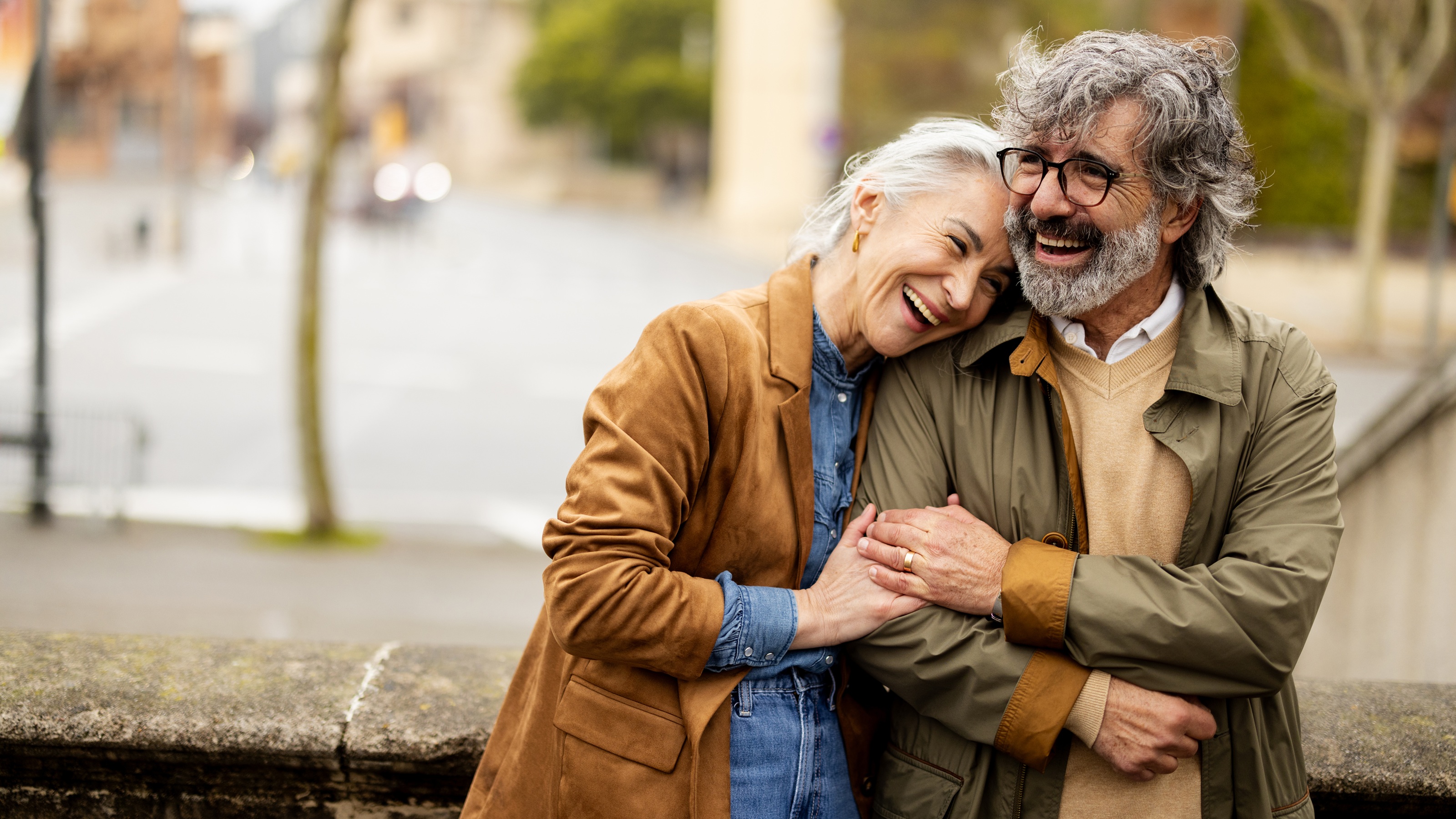 An older couple smile and laugh together on a city street.