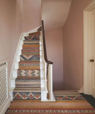 Stairwell with pink walls and patterned carpet running up stairs