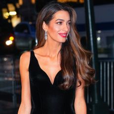 Amal Clooney is photographed wearing a long black velvet dress with diamond earrings.