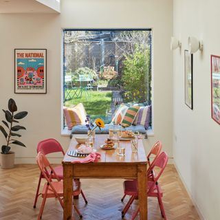 Kitchen dining area with wooden table, pink folding seats and oriel window looking over the garden