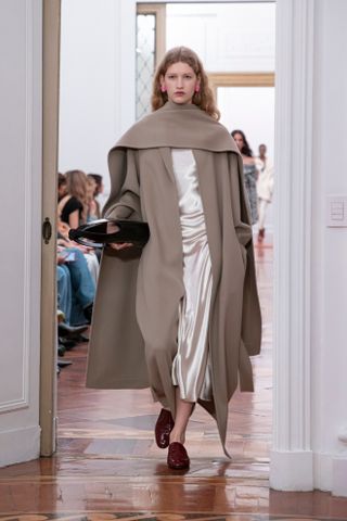 A model wearing a tan scarf coat and champagne-colored slip dress with red slippers walking in the Alberta Ferretti show during Milan Fashion Week.