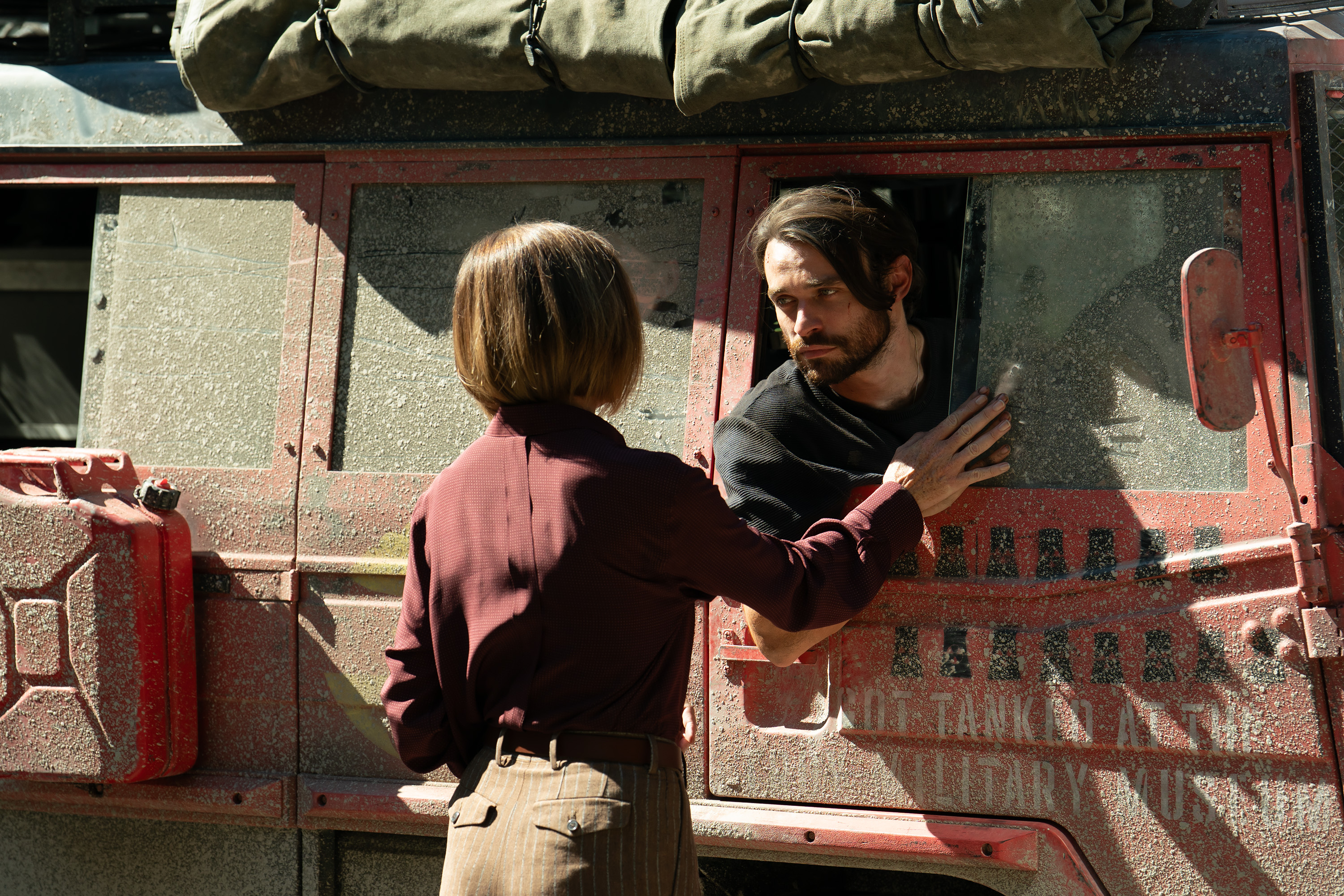 A woman (Julianne Nicholson as Sinatra) talks to a man (Thomas Doherty as Link) leaning out the window of a dirty Jeep, in a still from 'Paradise' season 2.