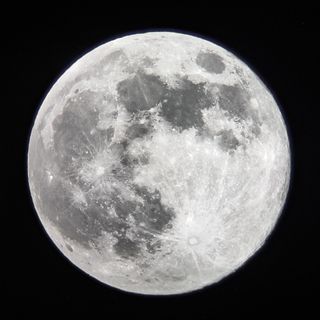 full snow moon shines bright with detailed craters against the black background of space.