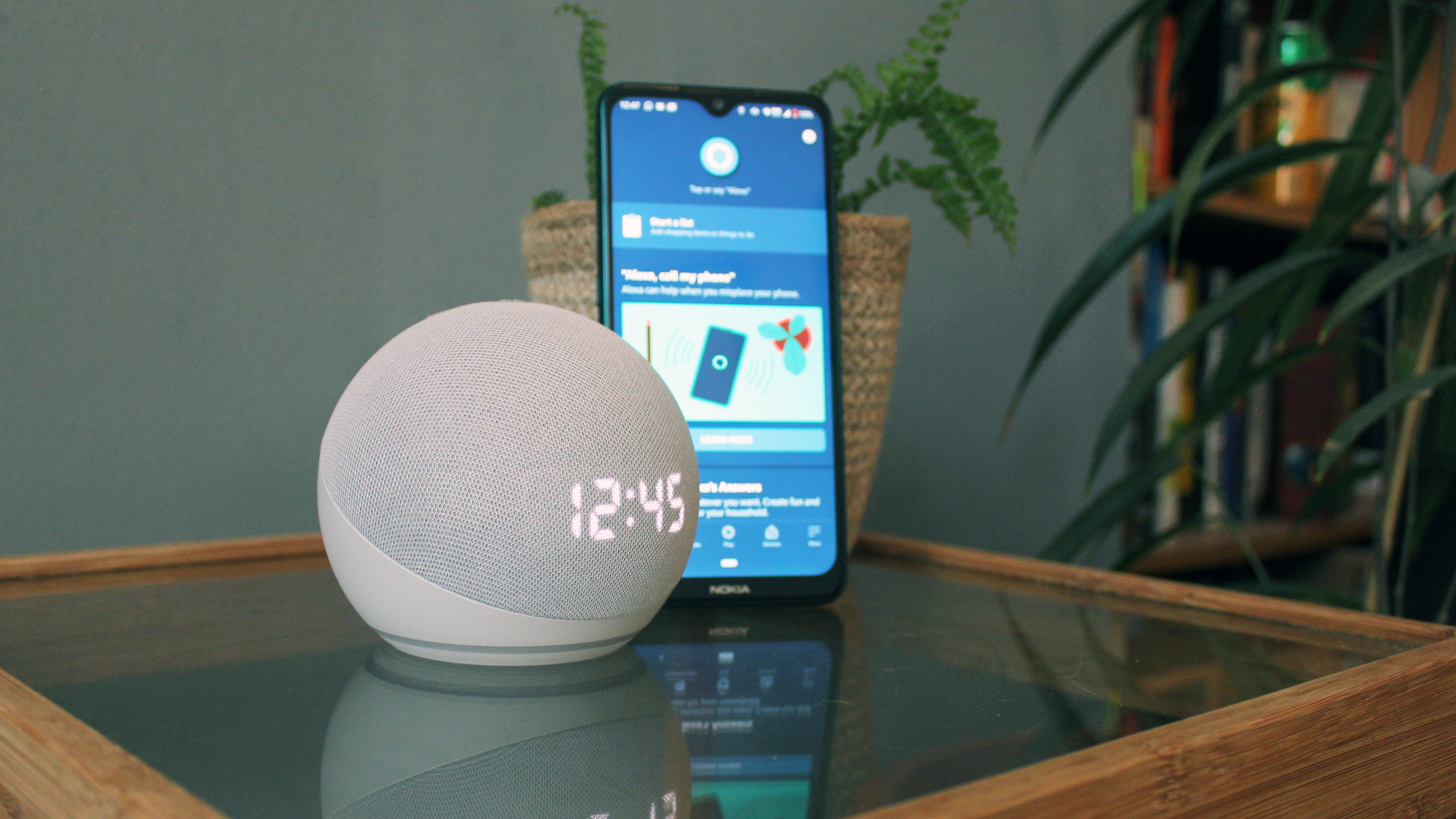the amazon echo dot with clock pictured next to a smartphone on a glass table