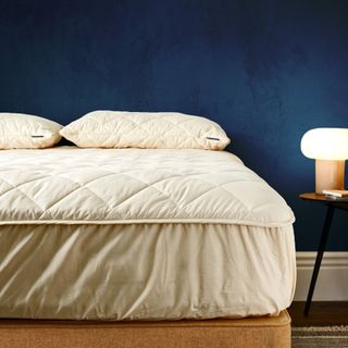 Woolroom mattress protector on a bed in a bedroom with navy blue walls