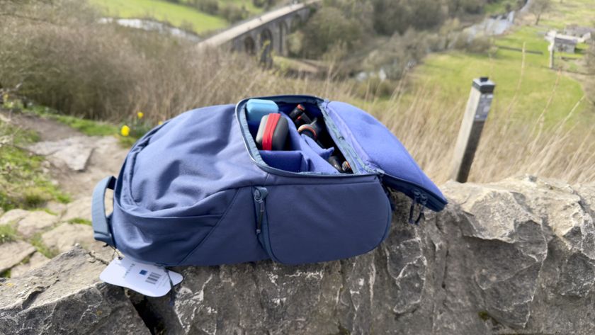 Shot of the backpack resting on a wall in the countryside. The top flap has been unzipped to reveal some of the backpacks contents